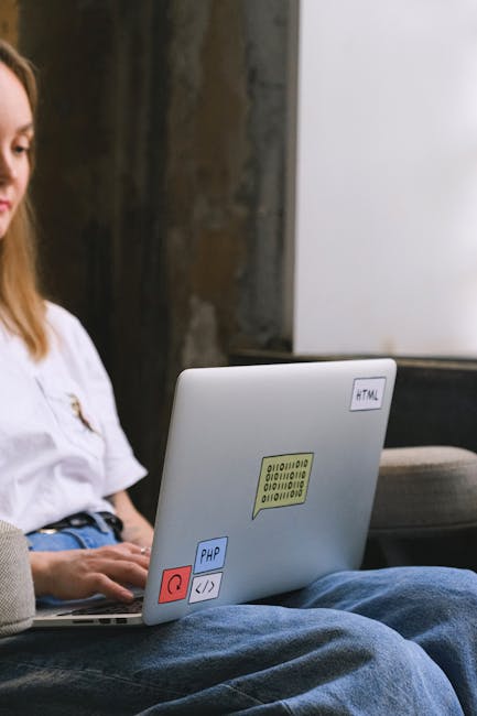 A person wearing a light blue shirt is seated at a desk with a white surface, actively engaged in a home relocation or packing process. They are holding a pen in one hand and pointing at a laptop scre