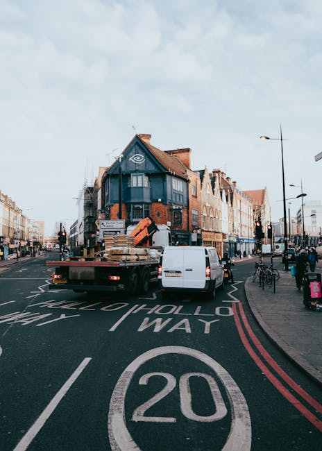 A street scene in Hammersmith featuring multi-storey buildings with a mixture of brick and ornate facades, visible on a clear day with good natural lighting. In the foreground, a white removals truck 